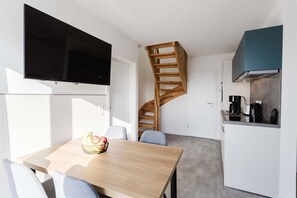 Eine kleine Küche mit einer Holztreppe, einem Esstisch mit Stühlen und einem an der Wand befestigten Flachbildfernseher.