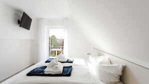 Ein Hotelzimmer mit Bett, weißer Bettwäsche, einem an der Wand montierten Fernseher und einem Balkon mit Blick.