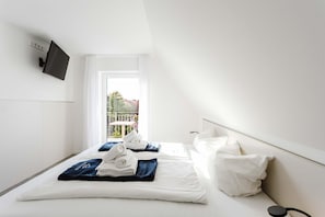 A hotel room with a bed, white bedding, a TV mounted on the wall, and a balcony with a view. - MEERholung Vacation Rental 4.2 – 2-Bedroom Penthouse Apartment with Rooftop Terrace - (Cuxhaven)