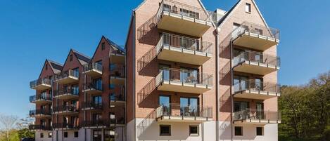 A multi-story residential building with balconies, a brick facade, and a clear sky.