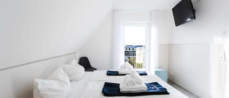 Habitación de hotel con cama, una silla, televisor y ventana con vista a edificios.