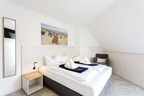 A modern hotel room with a bed, a chair, a desk, and a painting of a beach scene. - MEERholung Vacation Rental 4.5 - Two-level penthouse near the beach with a rooftop terrace - (Cuxhaven)