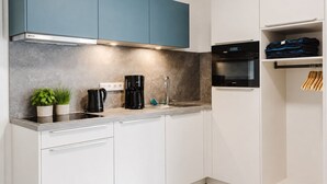 Cozinha moderna com armários brancos, um armário superior azul, uma cafeteira, uma pia e um forno preto.