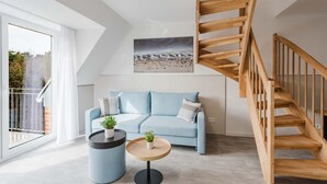Uma sala de estar moderna com um sofá azul claro, uma mesa de centro redonda, uma pequena planta em vaso e uma escada de madeira.
