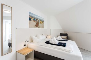 A modern hotel room with a bed, a bedside table, a wall-mounted painting, and a large mirror. - MEERholung FeWo 4.5 - Penthouse close to the beach on two levels with roof terrace - (Cuxhaven)