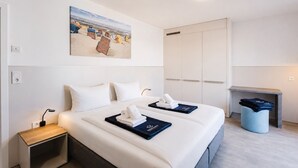 A hotel room with a bed, bedside tables, a painting, a wardrobe, and a small seating area. - MEERholung Vacation Rental 3.1: Beachfront Studio with Balcony - MEERholung House (Cuxhaven)
