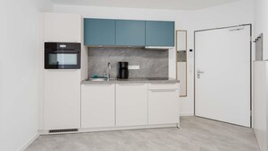 A compact kitchen with white cabinets, a black oven, a coffee maker, and a teal upper cabinet. - MEERholung Vacation Rental 3.1: Beachfront Studio with Balcony - MEERholung House (Cuxhaven)