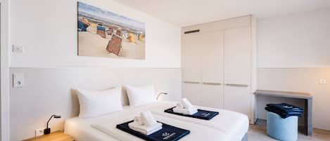 A hotel room with a bed, bedside tables, a painting, a wardrobe, and a small seating area.
