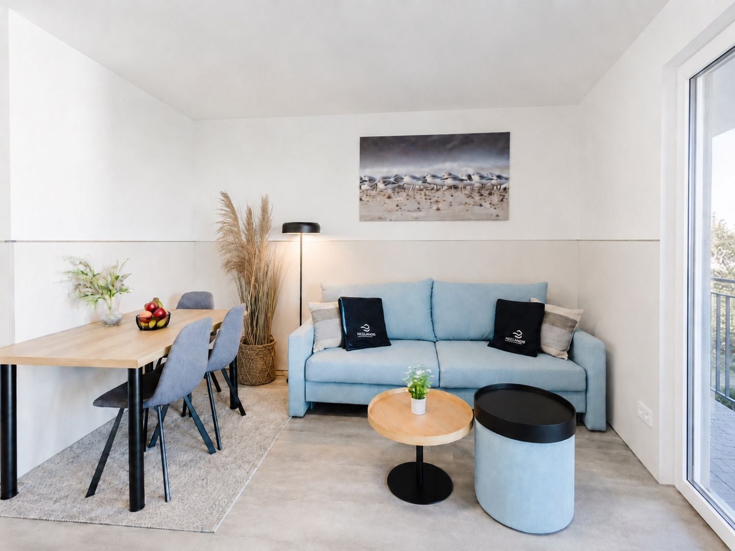 En moderne stue med sofa, rundt sofabord, spisebord med stole og et stort vindue.