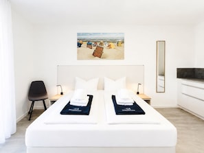 A hotel room with a large bed, a chair, a desk, a mirror, and a beach scene painting on the wall. - MEERholung apartment 2.2: for up to 4 people, approx. 400 m to the sea - MEERholung (Cuxhaven)