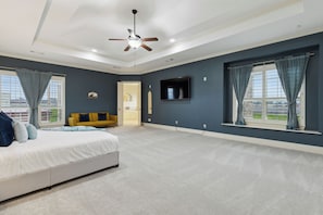 A bedroom with a bed, a ceiling fan, a TV mounted on the wall, and a window with curtains.