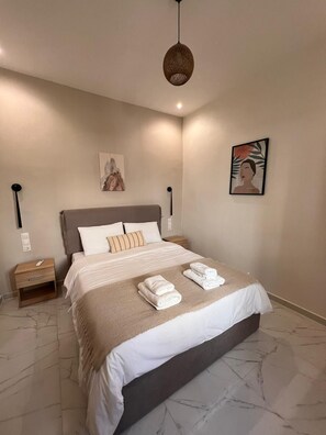 A modern hotel room with a large bed, a bedside table, a nightstand, a hanging light fixture, and two wall-mounted artworks. - Modh Patras - Modern Design Oasis in the City Centre (Patras)