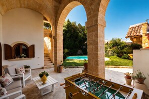An outdoor patio with a foosball table, a white sofa, and a pool in the background. - Villa Raffaella _ Spongano (Spongano)