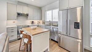 Una cocina moderna con electrodomésticos de acero inoxidable, una isla de madera y un taburete de bar.