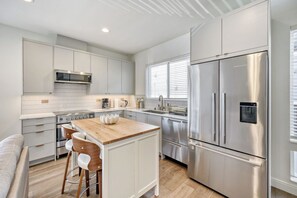 A modern kitchen with stainless steel appliances, a wooden island, and a bar stool. - Modern Townhome with Private Parking - Near Lumen Field, Downtown & Cap Hill (Seattle)