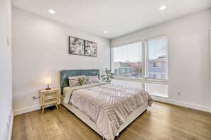 A bedroom with a bed, bedside table, lamp, artwork, and large windows. - Modern Townhome with Private Parking - Near Lumen Field, Downtown & Cap Hill (Seattle)