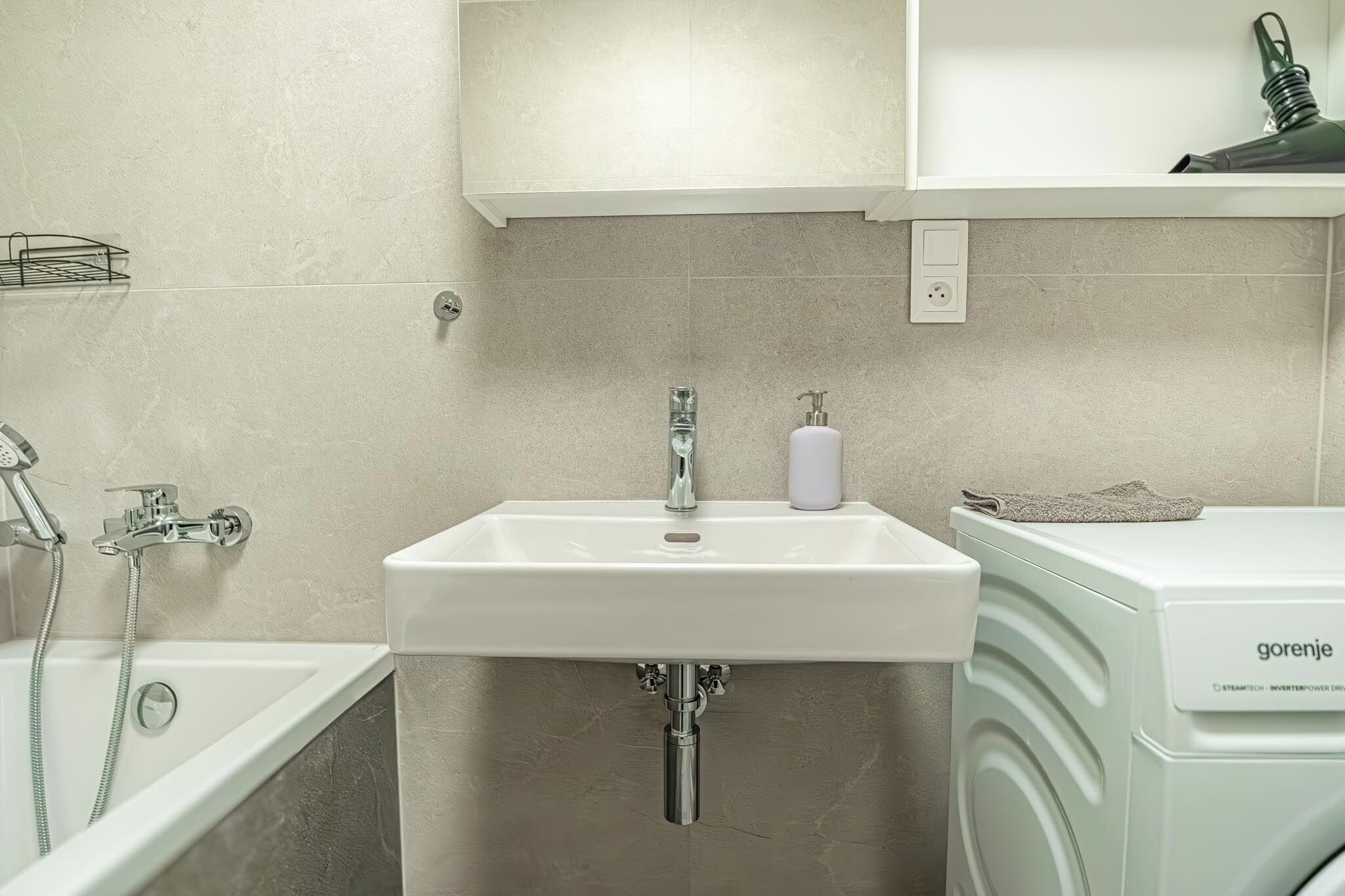 A bathroom with a white sink, a shower, and a washing machine.