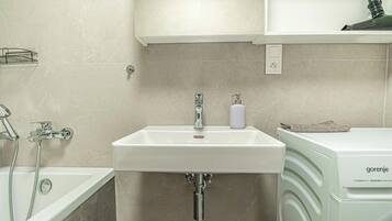 A bathroom with a white sink, a shower, and a washing machine.
