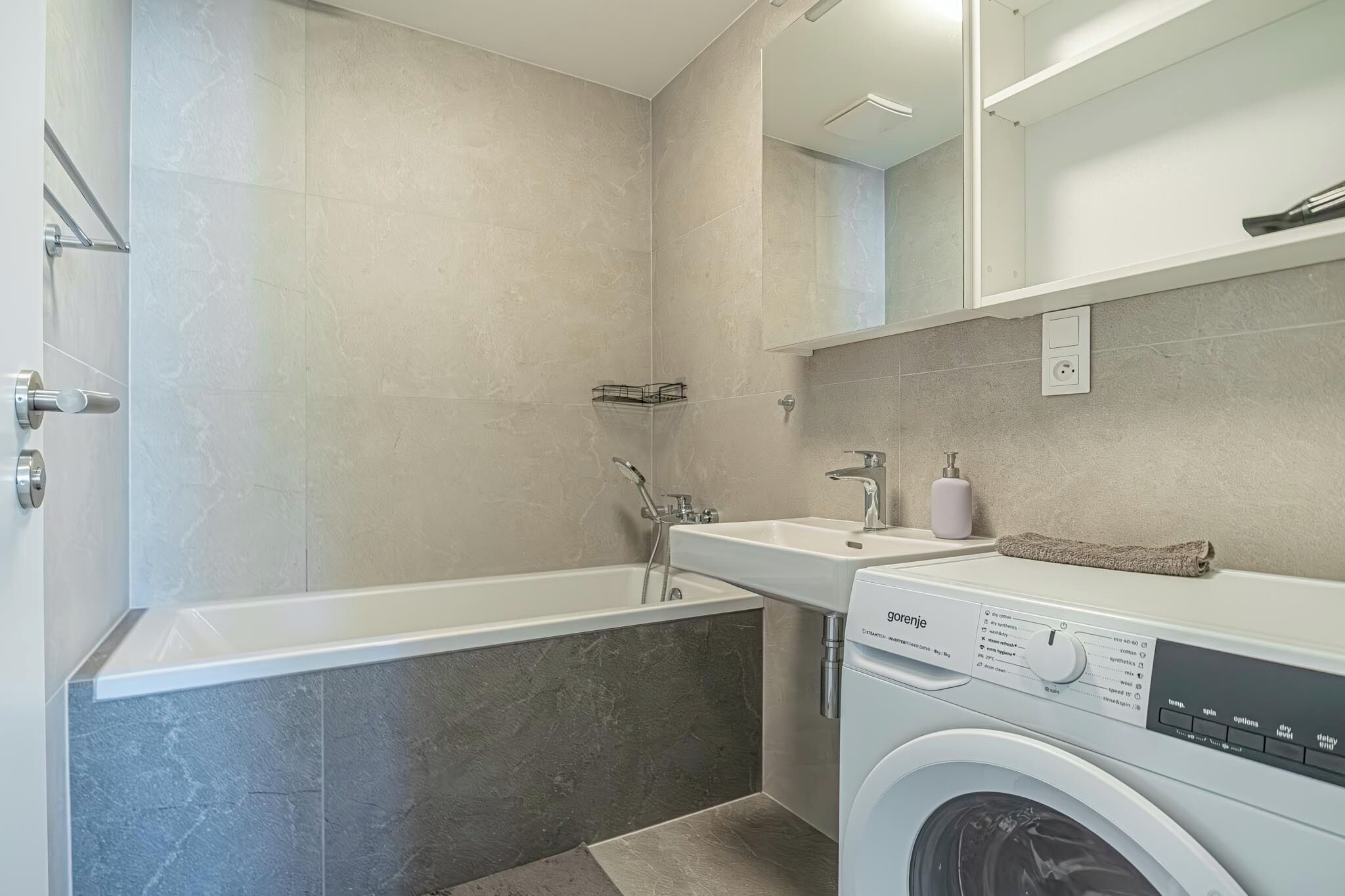 Une salle de bain moderne équipée d’une baignoire, d’un lavabo et d’un lave-linge.
