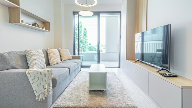 A modern living room with a sofa, a coffee table, a TV, and a sliding door leading to a balcony. - 1BR Apartment Near Airport with Parking (Bratislava)