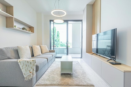 A modern living room with a sofa, a coffee table, a TV, and a sliding door leading to a balcony.