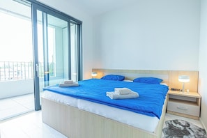 A modern bedroom with a large bed, bedside lamps, and a view through a sliding glass door. - 1BR Apartment Near Airport with Parking (Bratislava)