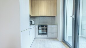 A modern kitchen with a built-in oven, white cabinets, and a large sliding glass door leading to an outdoor area. - 1BR Apartment Near Airport with Parking (Bratislava)