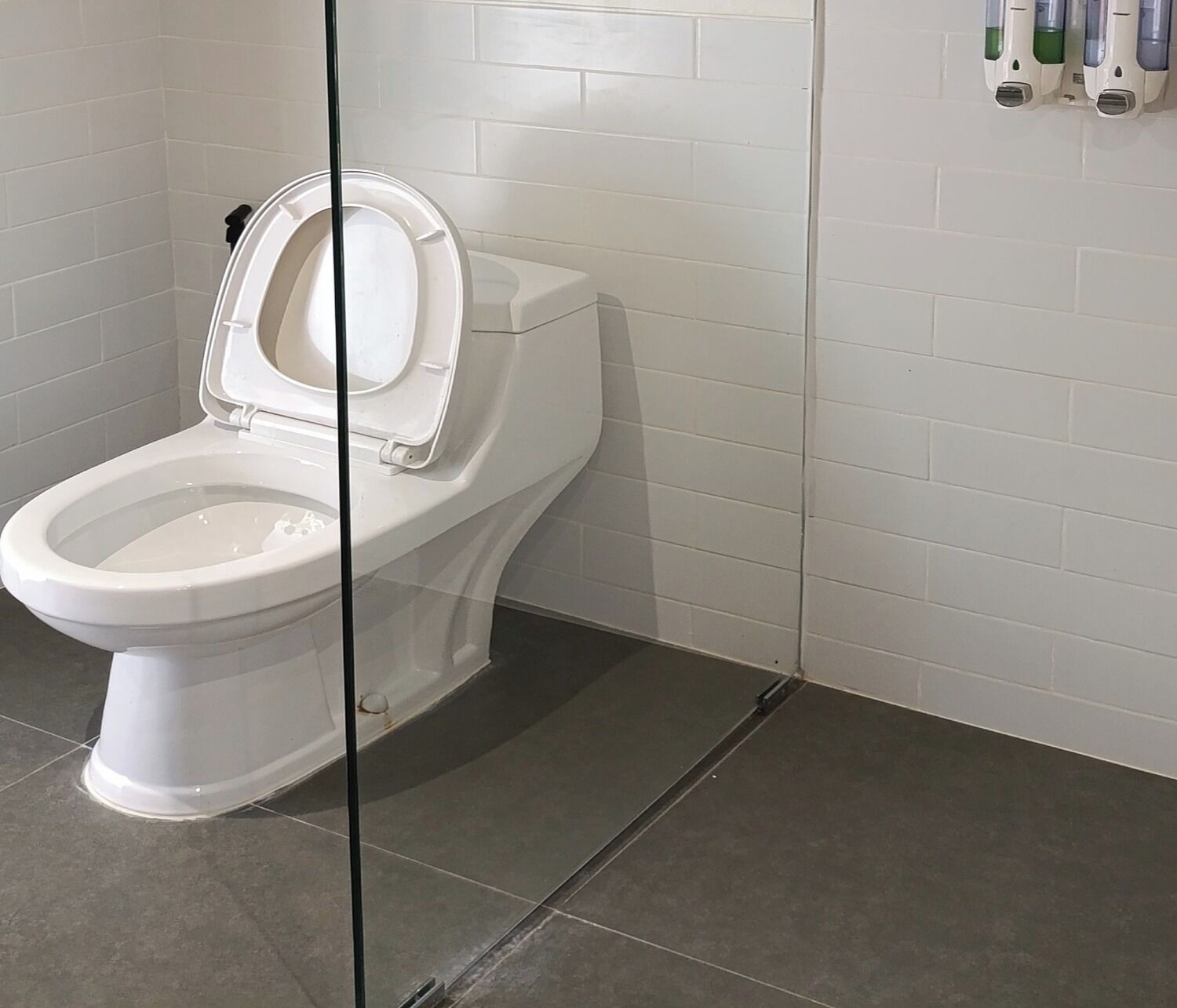 A white toilet with a closed lid in a bathroom with white tiled walls and dark floor tiles.
