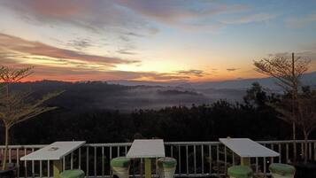A terrace with a table and chairs, a railing, and a view of a valley during sunset.