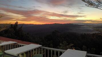 A balcony with a view of a sunset over a forested landscape.