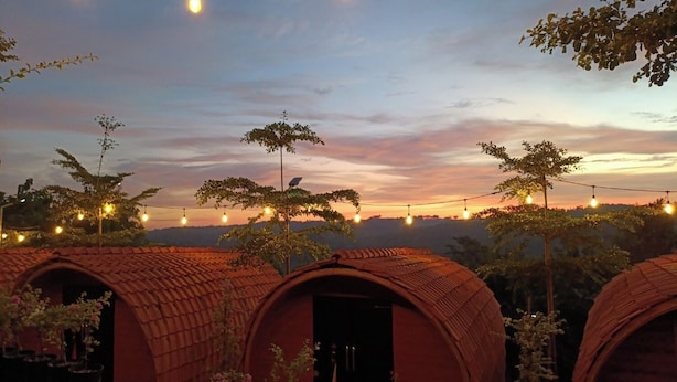 Una hilera de casas de campo con techos abovedados y luces colgantes, frente a un cielo al atardecer.