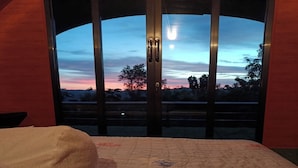 Un dormitorio con una cama, un ventanal con vista al cielo y una puerta.
