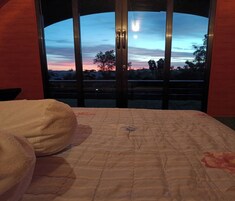 Um quarto com uma cama, uma janela com vista para o céu e uma porta.