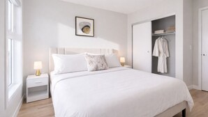 Een slaapkamer met een bed, nachtkastjes, een lijst met kunstwerk, een kledingkast met kleren en een raam.