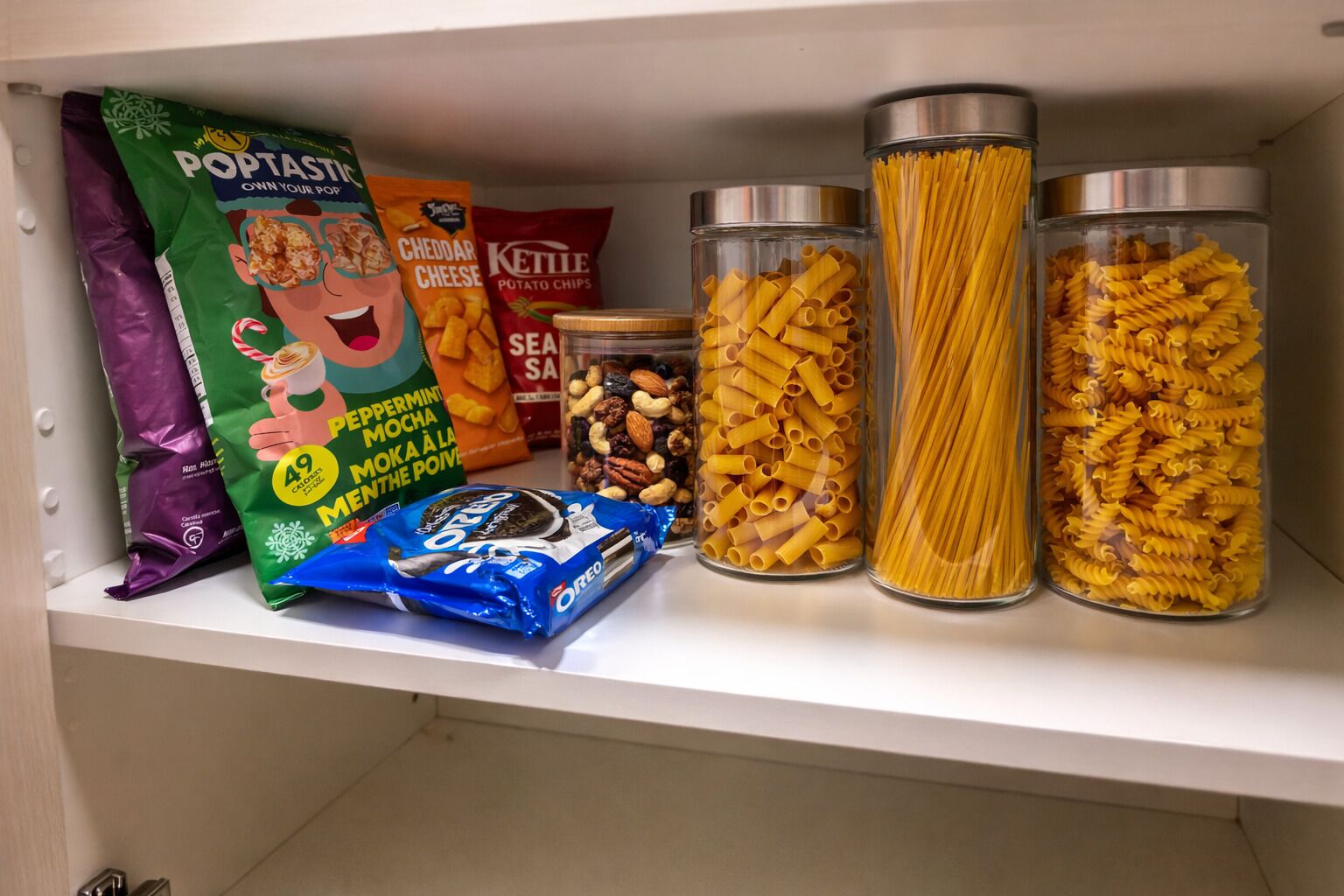 A pantry shelf with various food items including pasta, chips, and a bag of cookies.