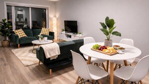 Een moderne woonkamer met een bank, een eettafel met stoelen, een televisie en een plant.