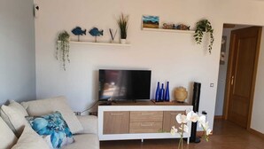 Een woonkamer met een bank, televisie en decoratieve items, waaronder sculpturen van vissen en een plant.