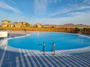 Une piscine avec deux échelles, une clôture en bois et des bâtiments en arrière-plan.