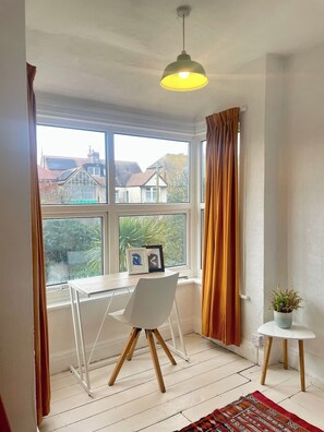 A room with a large window, a white desk, a chair, a hanging light fixture, and a small table with a plant. - Beautiful house close to beach, Dreamland, station (Margate)