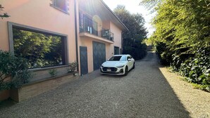 Una casa moderna de dos pisos con entrada de grava, un coche blanco estacionado al frente y un balcón en el piso superior.