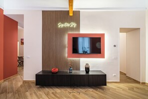 Een moderne woonkamer met een aan de muur bevestigde televisie, een houten paneel met een neonreclame en een zwarte entertainmentkast.