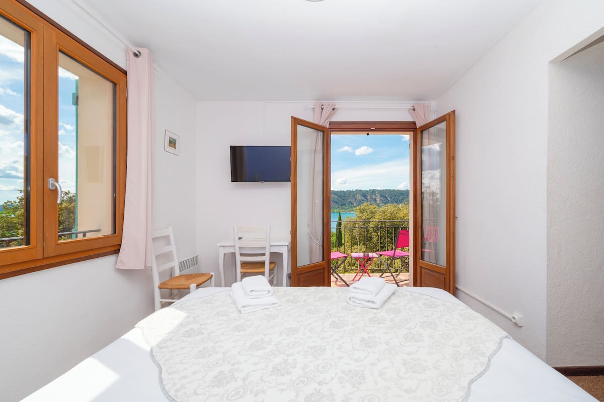 A bedroom with a bed, a chair, a TV, and a balcony with a view.
