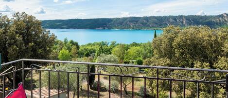 Un balcón con dos sillas rosadas y una mesa, con vista a un lago y colinas.