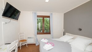 Habitación de hotel con cama, escritorio, silla, televisor montado en la pared y ventana con cortinas.