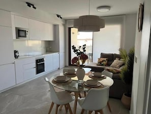 A modern kitchen with white cabinets, a microwave, and a dining area with a glass table and white chairs. - Apartment with rooftop pool 150 m from the beach (03193 San Miguel des Salinas)