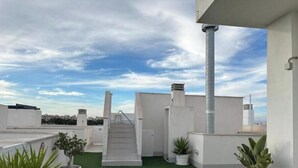 Terraza en la azotea con césped artificial, paredes blancas, una escalera de metal y plantas en macetas.