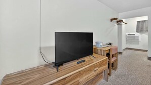 Ett rum med ett skrivbord i trä, en tv, en stol, ett litet bord och en väggmonterad luftkonditioneringsanläggning.