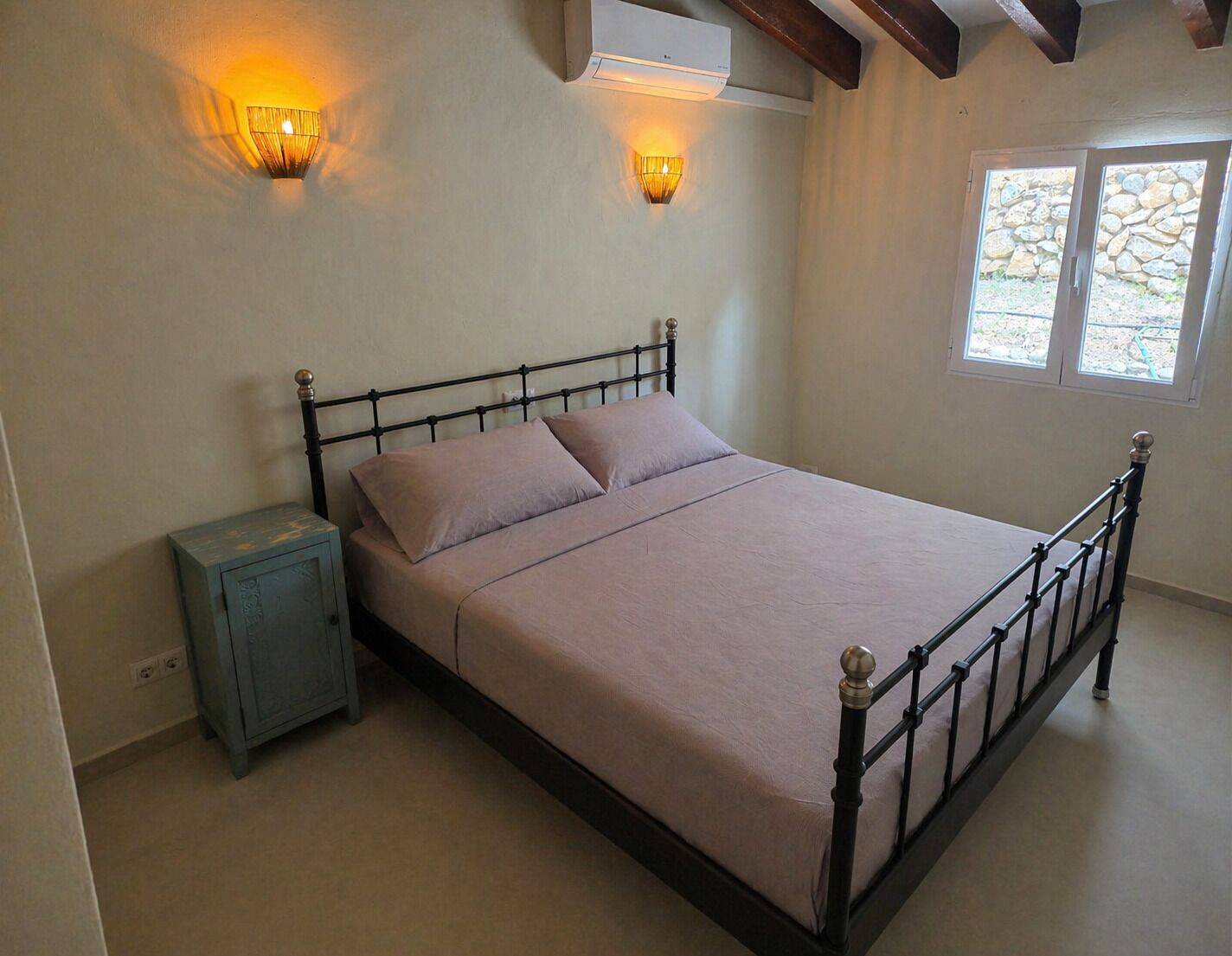 Quarto com cama, mesa de cabeceira, luminárias na parede e aparelho de ar condicionado.