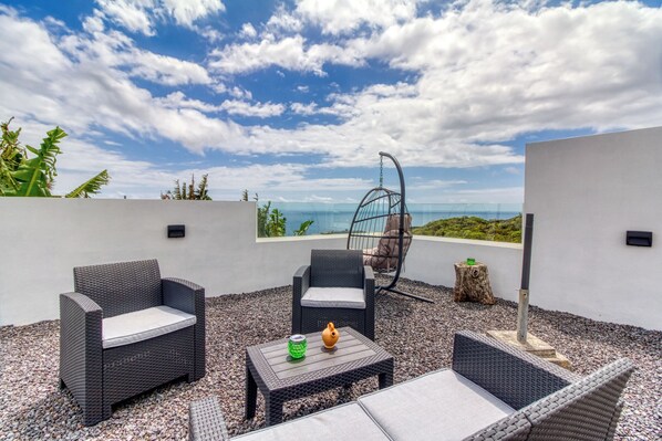 An outdoor seating area with wicker furniture, a hanging chair, and a view of the ocean.