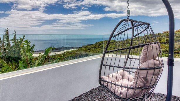 Una silla colgante con vista al océano y al verdor.